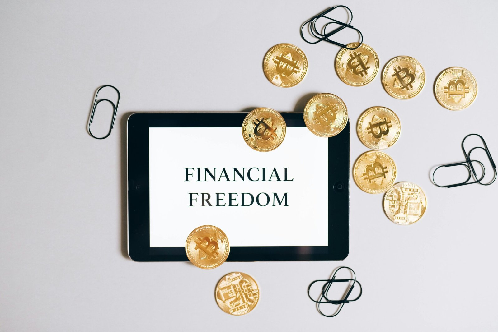 Top view of a tablet displaying 'Financial Freedom' with scattered bitcoin coins, symbolizing digital currency.